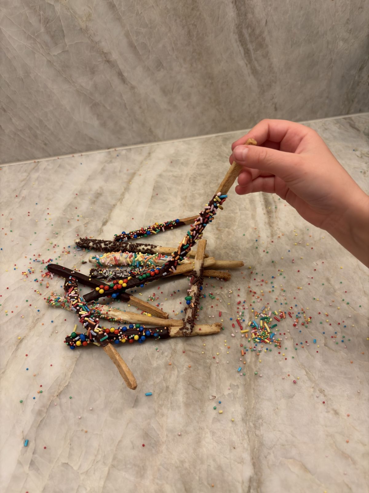 Une main d’enfant tient un bâtonnet au chocolat couvert de vermicelles
